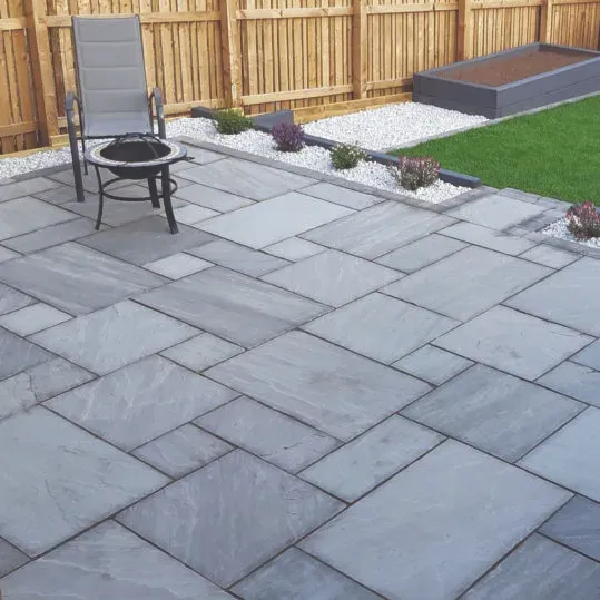 A modern grey paving slab patio with garden furniture, set in a neat garden with a lawn and wooden fence.
